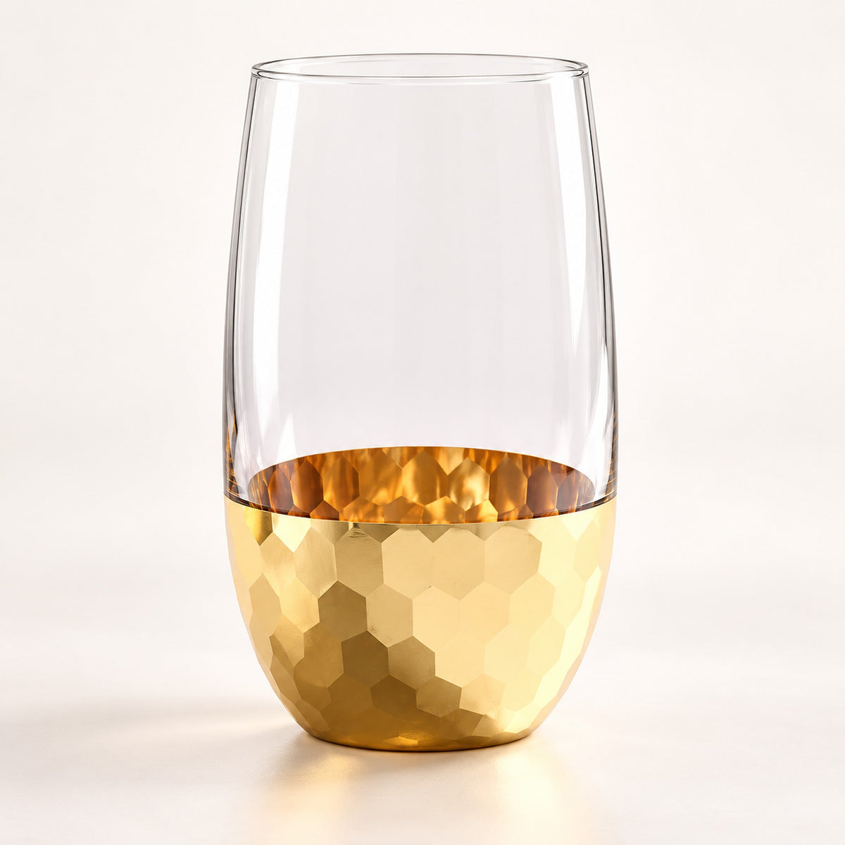 A clear stemless wine glass with a hammered gold metallic finish at the bottom, shown on a clean white background.