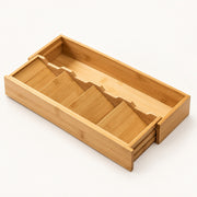 A bamboo drawer organizer with multiple angled compartments, shown partially open on a clean white background.