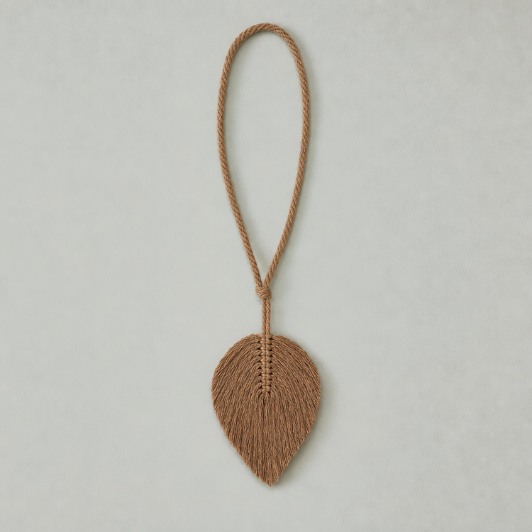 A natural brown woven rope ornament shaped like a leaf, suspended from a matching braided rope loop, displayed against a neutral light gray background.