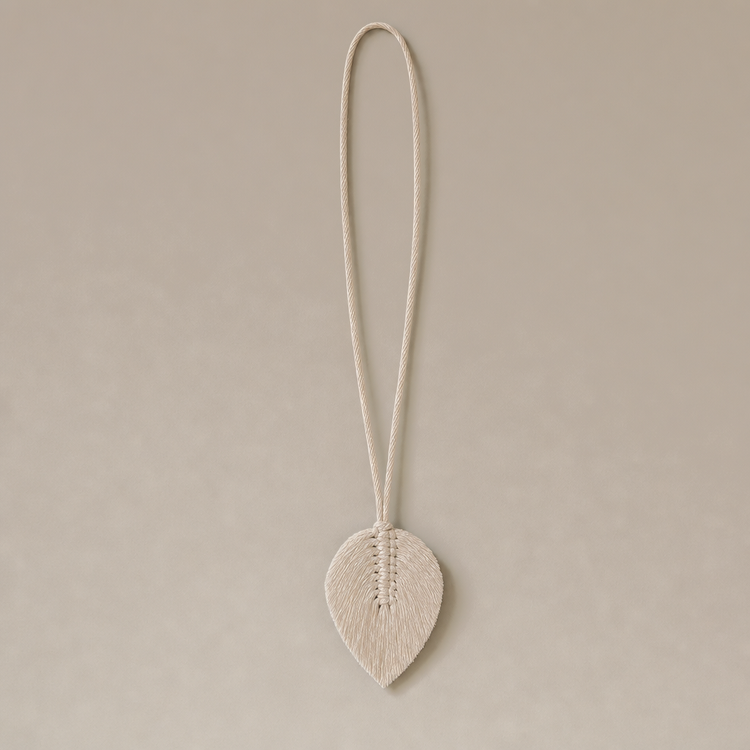 A gray curtain tied back with a cream-colored rope tie and a matching leaf-shaped decorative clip, shown against a plain off-white background.