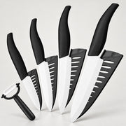 A 5-piece kitchen knife set with black handles and white blades, shown with matching black sheaths and a black-handled peeler on a light gray background.