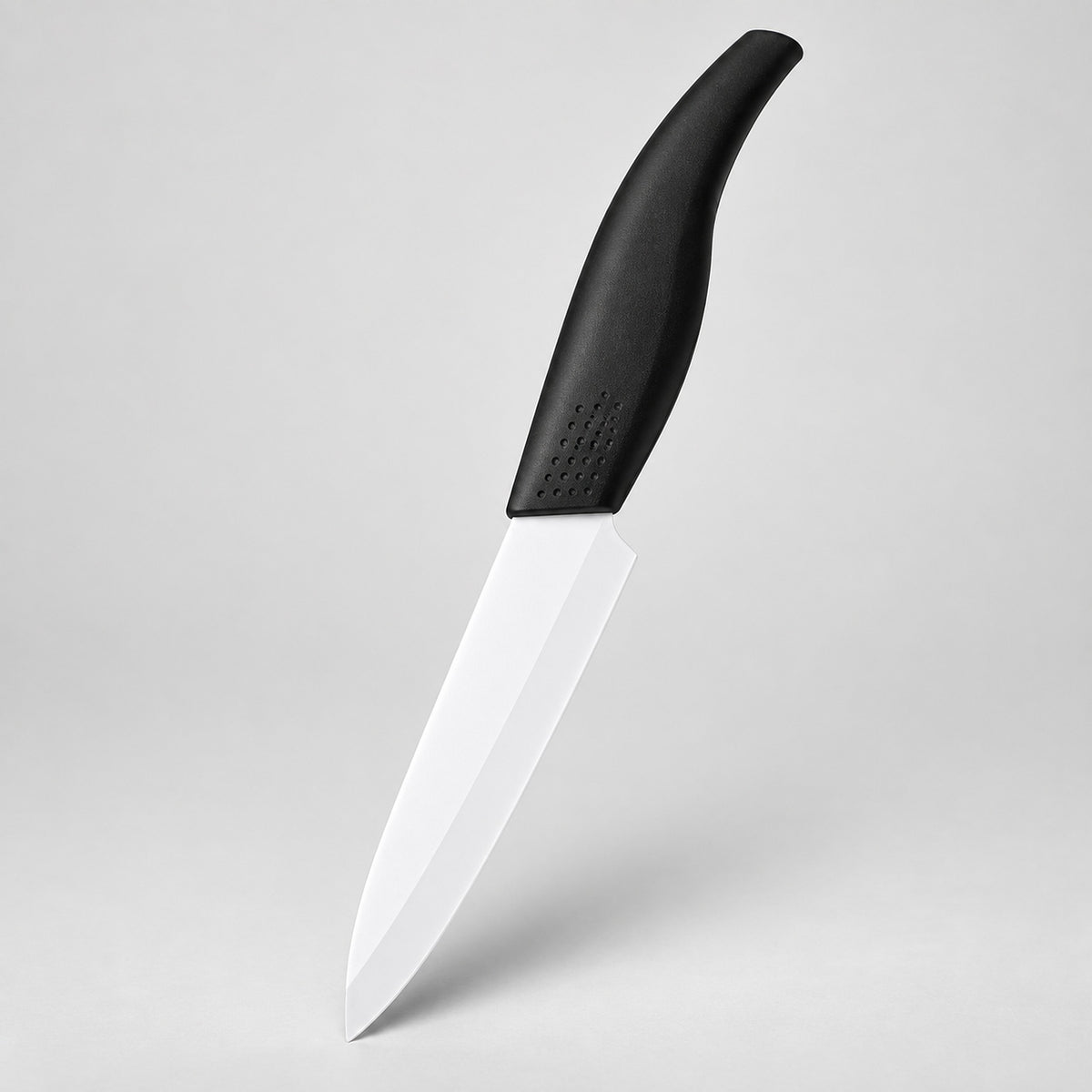 A kitchen knife with a white blade and a black ergonomic handle, shown floating against a light gray studio background.