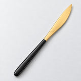 One black and gold dinner knife on a soft studio background.