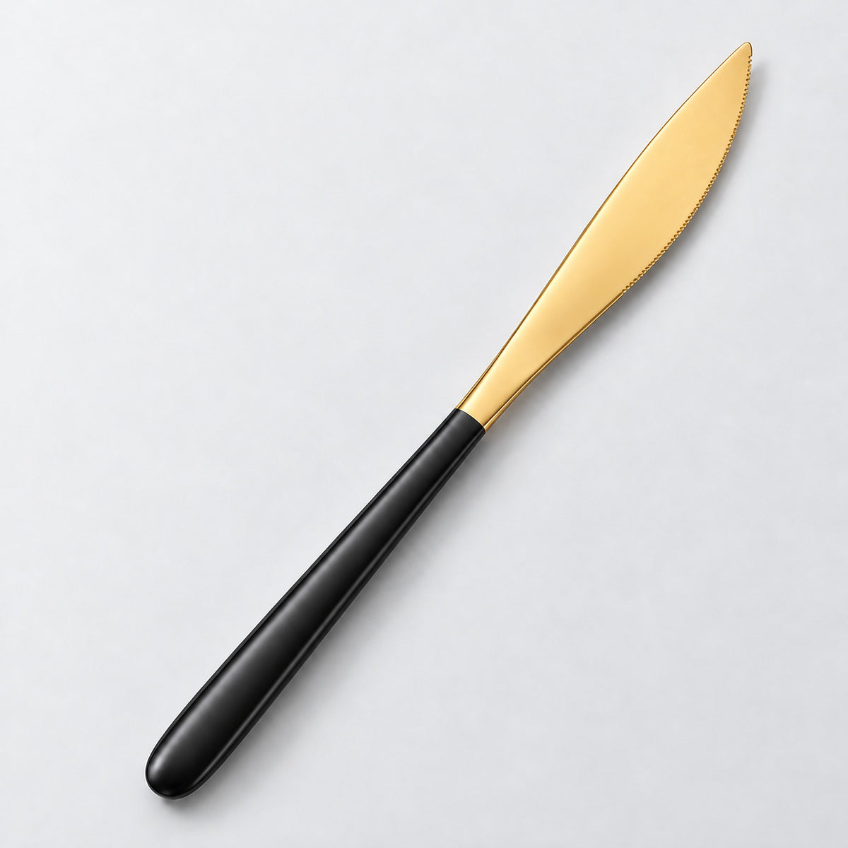 One black and gold dinner knife on a soft studio background.