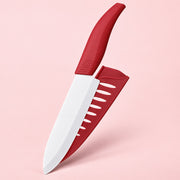 A red and white kitchen knife shown diagonally with its matching red sheath on a solid light pink background.