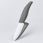 A kitchen knife with a matte gray handle and a silver blade featuring a serrated gray edge, shown floating against a light gray background.