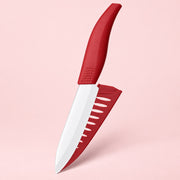 A red and white kitchen knife with a matching red sheath, shown against a solid light pink background.