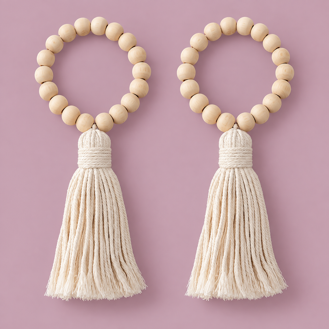 Two matching beaded tassel keychains on a solid dusty pink background. Each keychain features a circle of light natural wood beads with a thick cream-colored cotton rope tassel hanging below.