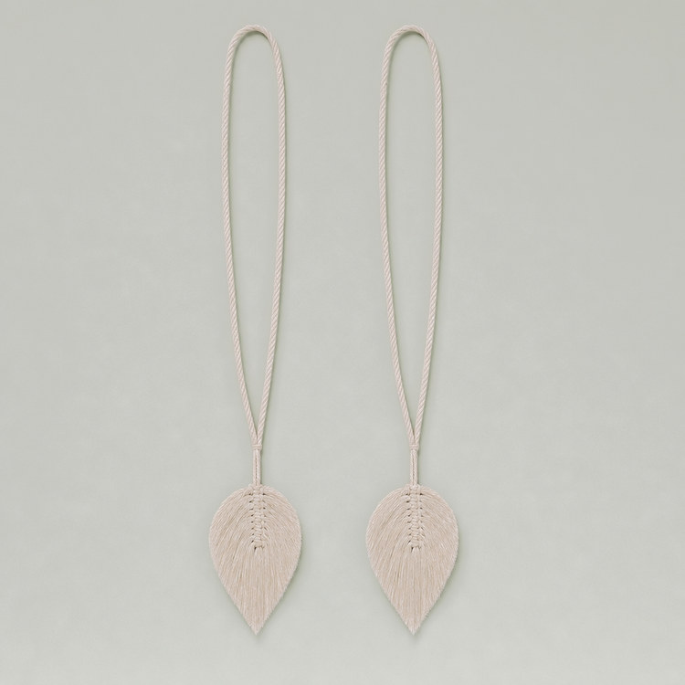 A pair of long, minimalist drop earrings with textured, leaf-shaped pendants suspended from thin braided cords, shown against a solid light gray background.