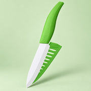 A small kitchen knife with a bright green ergonomic handle and matching green sheath, shown floating against a pale green studio background.