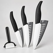Four kitchen knives and a peeler with black handles and white blades, arranged on a light gray background.