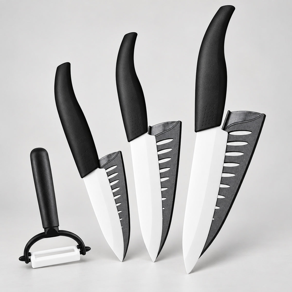 Four kitchen knives and a peeler with black handles and white blades, arranged on a light gray background.