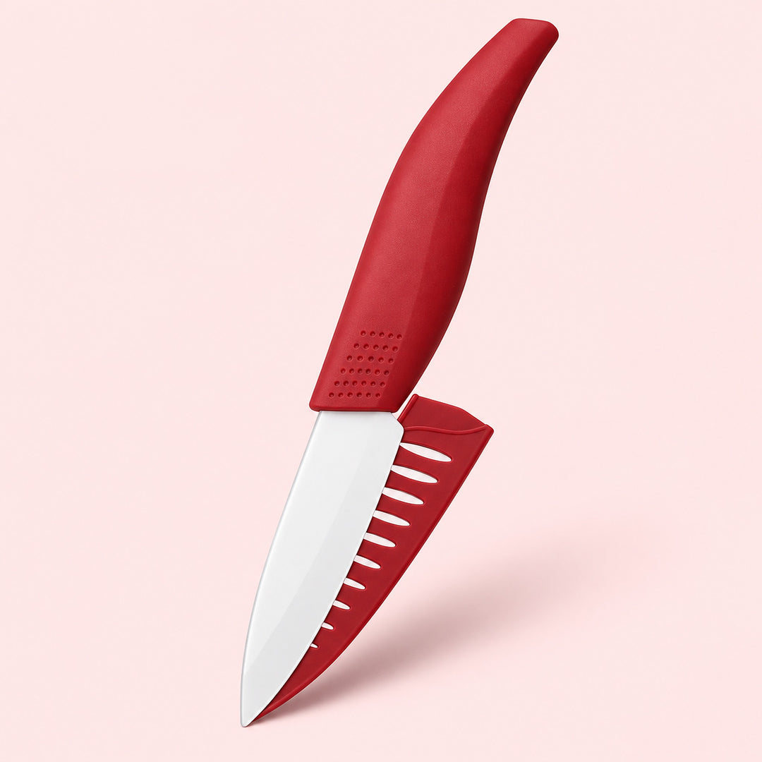 A red and white kitchen knife with a matching red protective sheath, shown floating against a solid pale pink background.