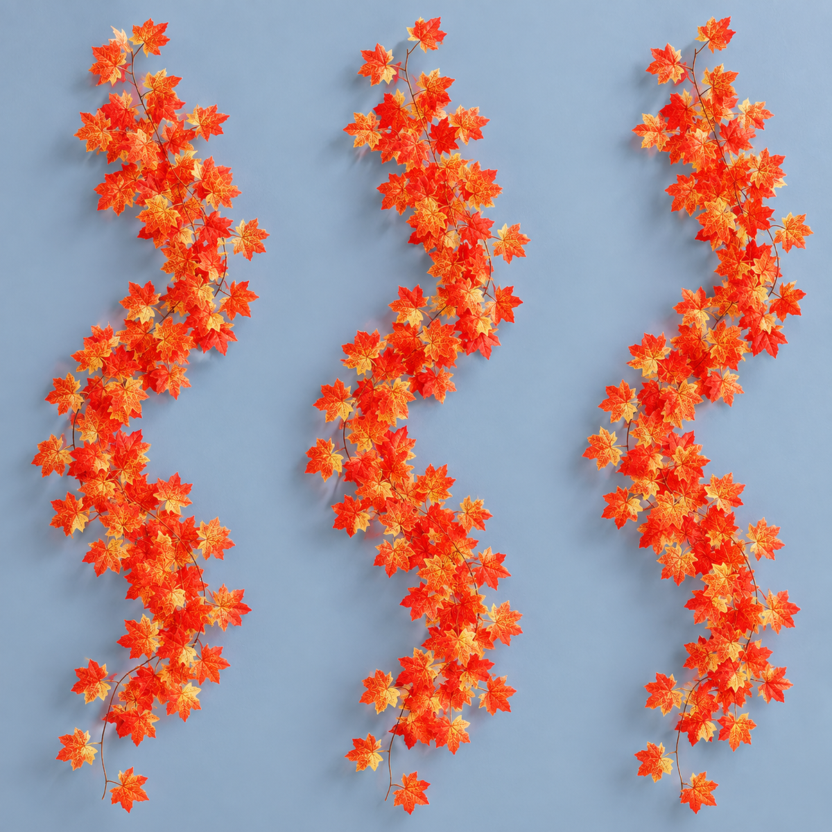 Three artificial maple leaf garland strands hung together on a pale blue wall