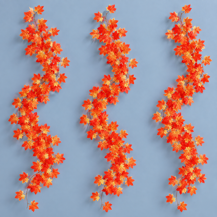 Three artificial maple leaf garland strands hung together on a pale blue wall