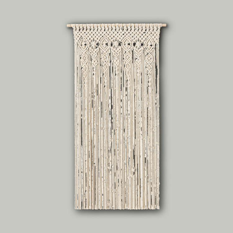 A cream-colored macrame wall hanging with intricate woven geometric patterns at the top and long hanging cords below, displayed against a plain off-white wall.