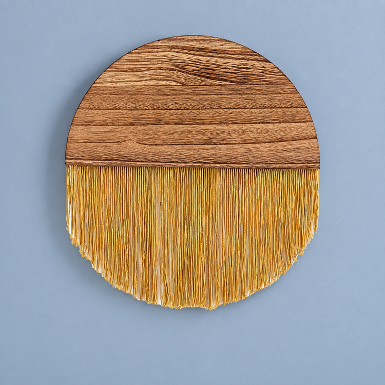 Mustard gold fringe circle with a wood top half on a blue painted wall