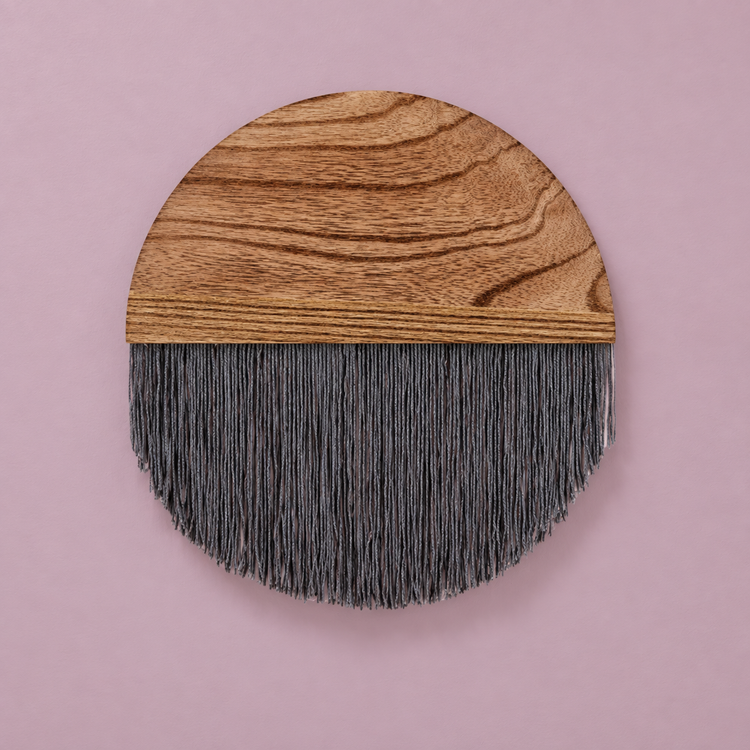Slate gray fringe under a grained wood half circle against a dusty pink wall