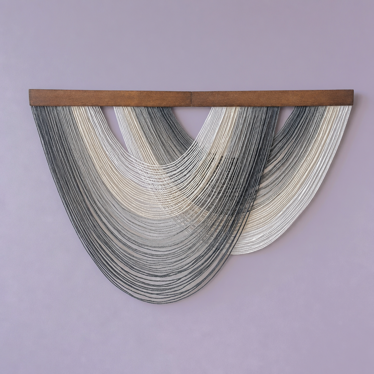 A modern wall hanging sculpture featuring two semi-circular strands of thin, dark gray and off-white cords suspended from a horizontal wooden bar, set against a solid lavender wall.