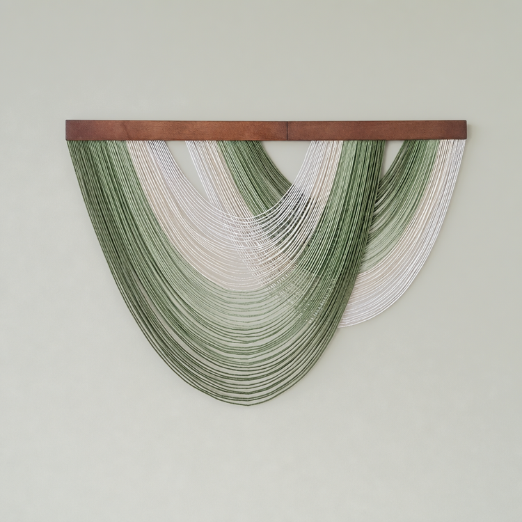 A wall-mounted decorative textile wall hanging with a rectangular wooden top bar and multiple draped strands in green and white forming an arch shape against a plain light gray wall.