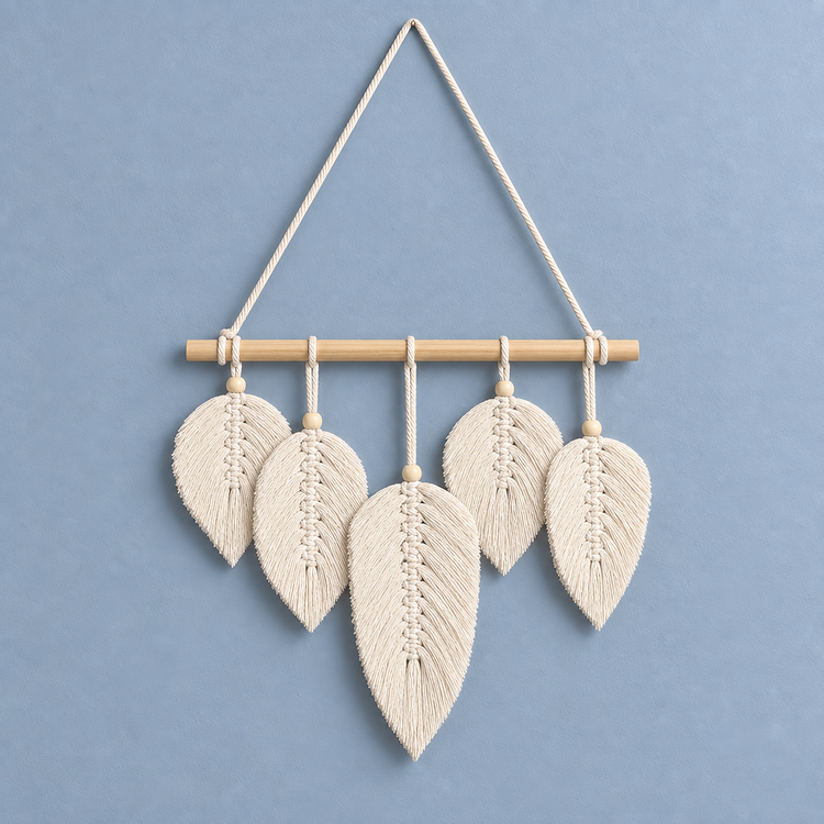 Five cream combed macrame leaves on a wooden dowel against a soft blue wall
