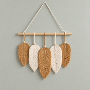 Five tan and cream combed macrame leaves hung from a wooden dowel on a sage wall