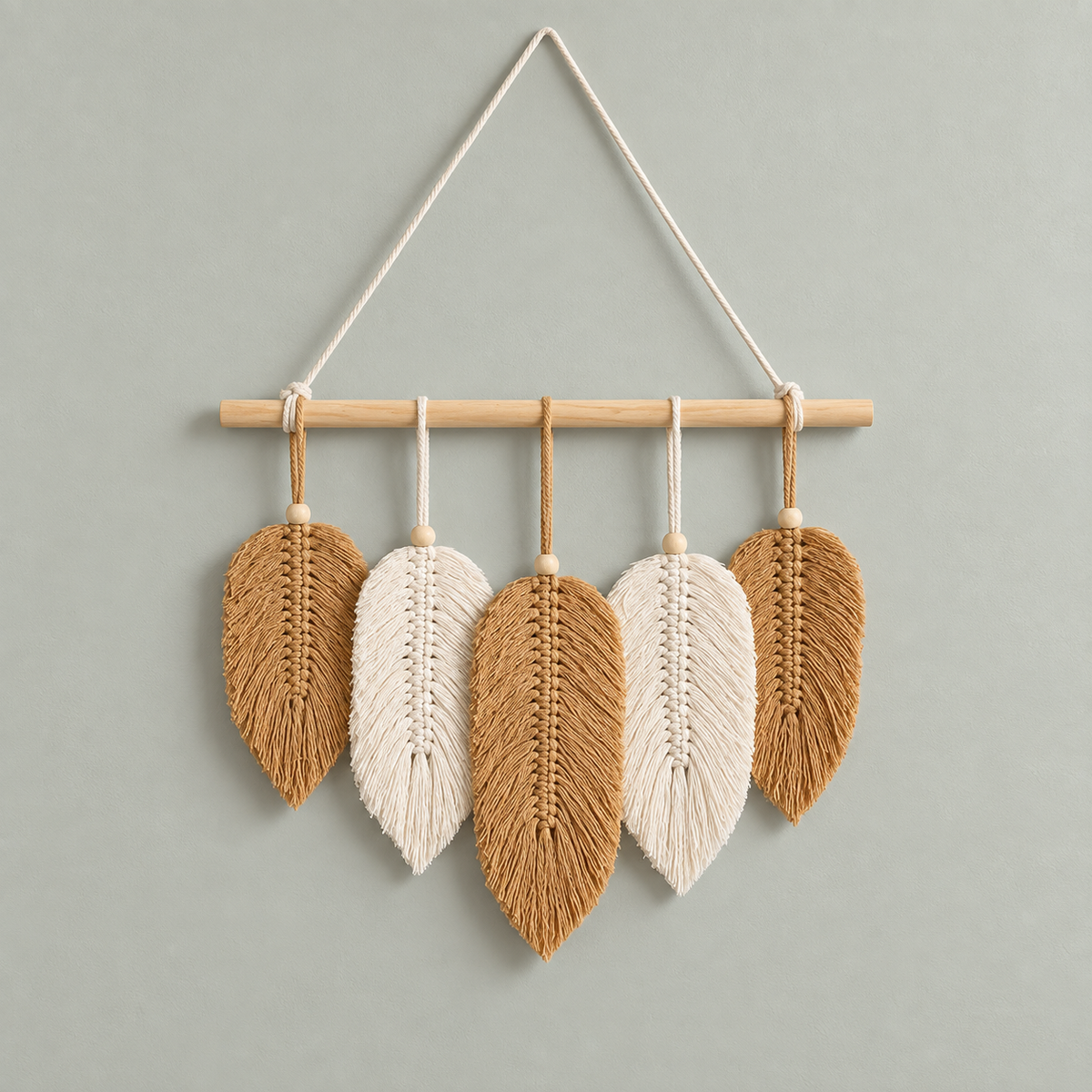 Five tan and cream combed macrame leaves hung from a wooden dowel on a sage wall
