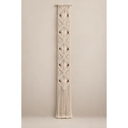 Off-white knotted macrame banner with stacked diamonds on a warm gray wall