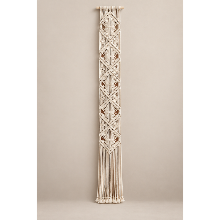 Off-white knotted macrame banner with stacked diamonds on a warm gray wall