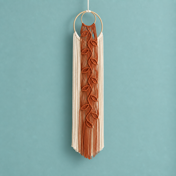Rust orange knotted leaf vine on cream cord hanging from a wooden ring, teal wall