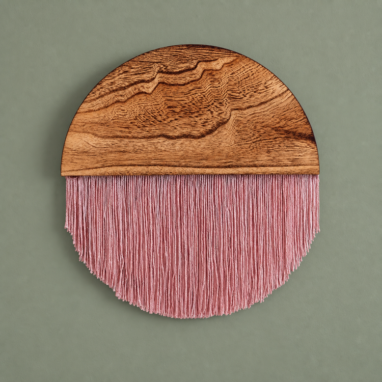 Dusty rose fringe under a figured wood half disc on a sage green wall