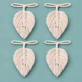 Four identical cream-colored macrame leaf ornaments with hanging loops, arranged in a 2x2 grid on a solid teal background.