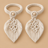 Two matching cream macrame hair ties with leaf-shaped tassels and wooden button centers, displayed on a solid beige background.