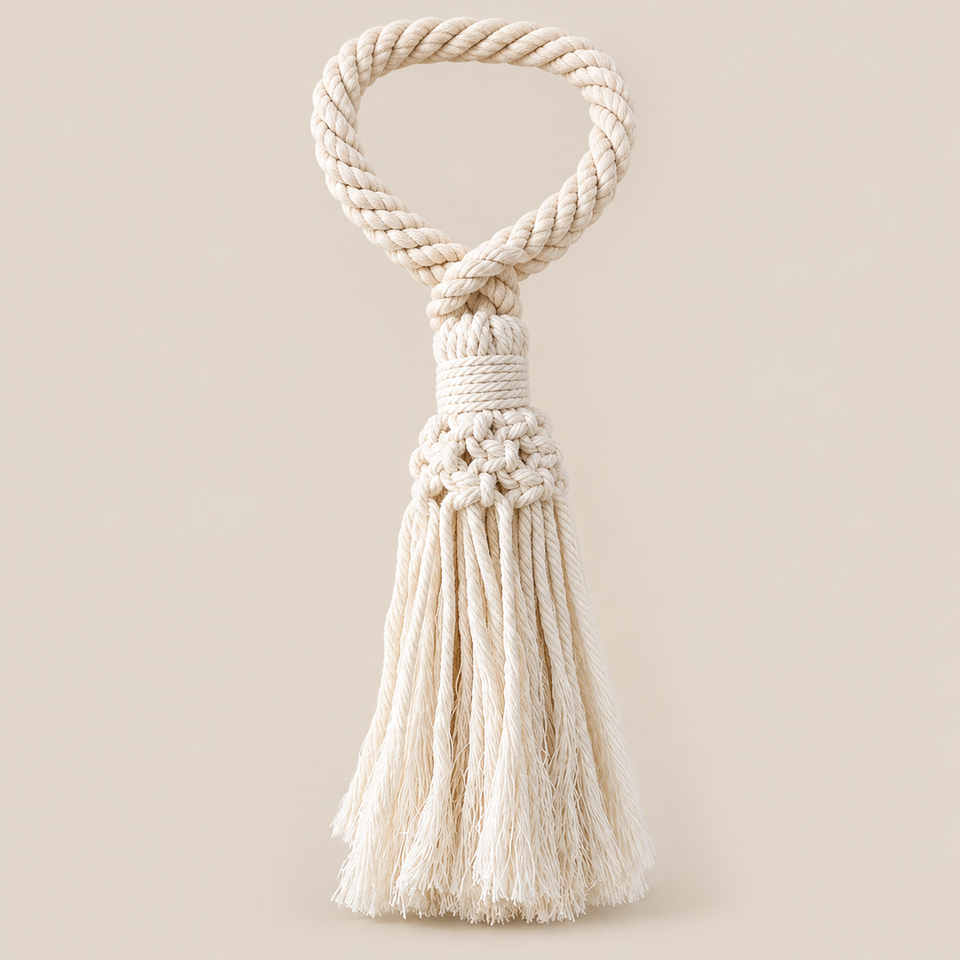 A cream-colored cotton rope tassel ornament with a knotted handle, shown against a solid beige background.