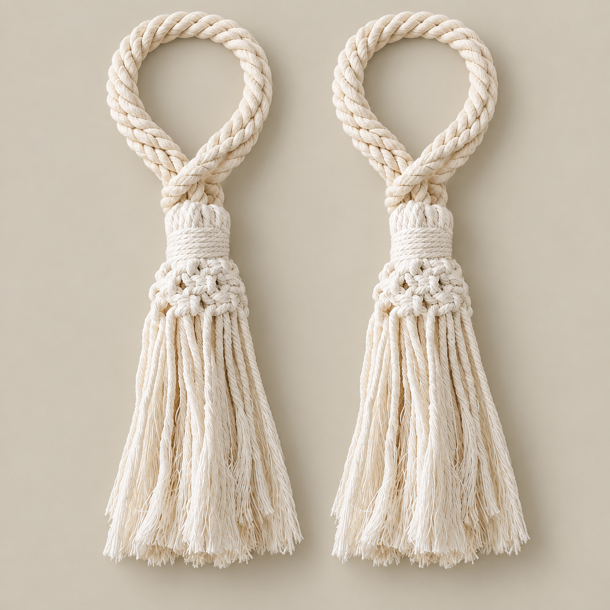 Two matching cream macrame tassel keychains with braided rope loops and knotted tassels, displayed on a solid beige background.
