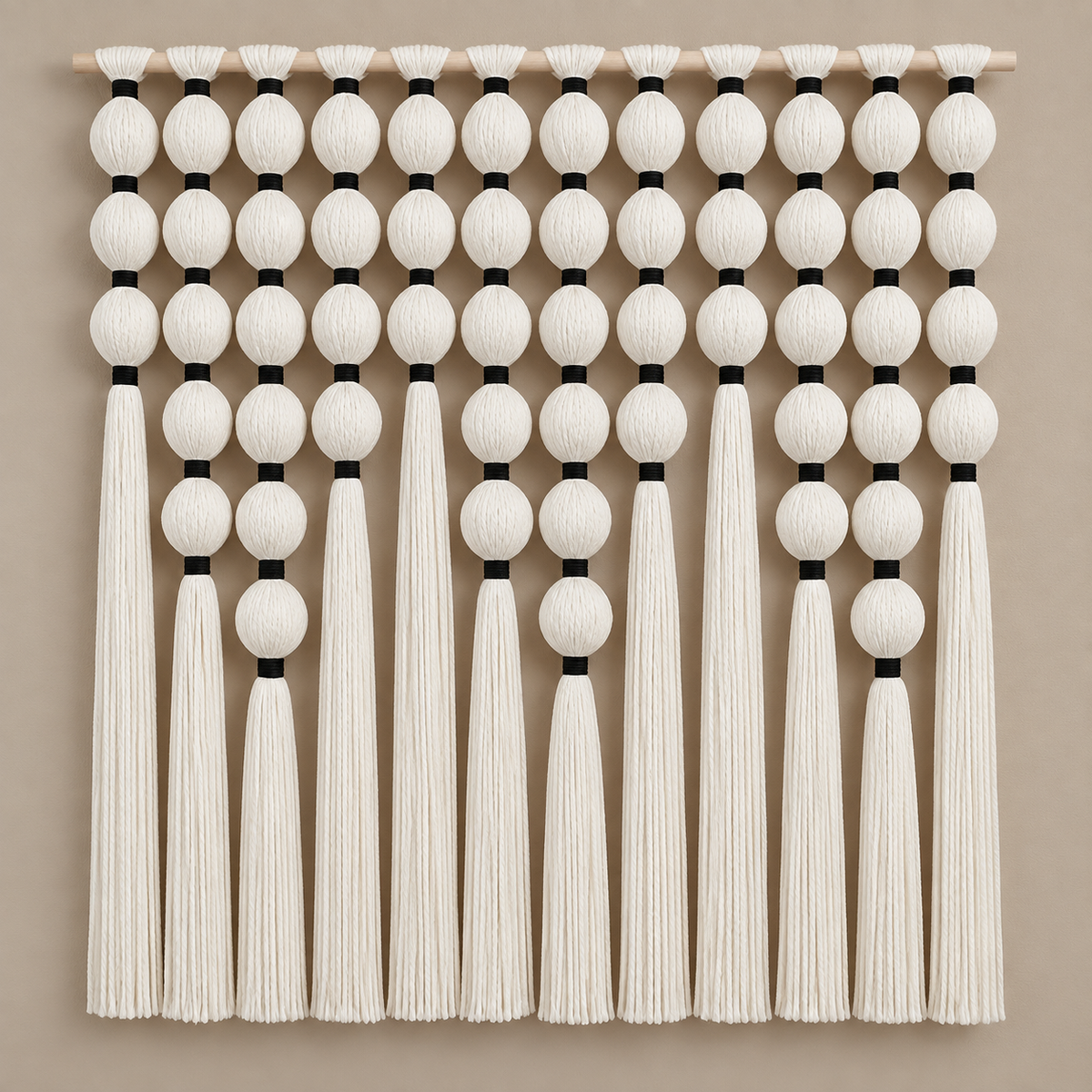 Grid of cream wound yarn spheres with black bindings and long tassels on a warm wall