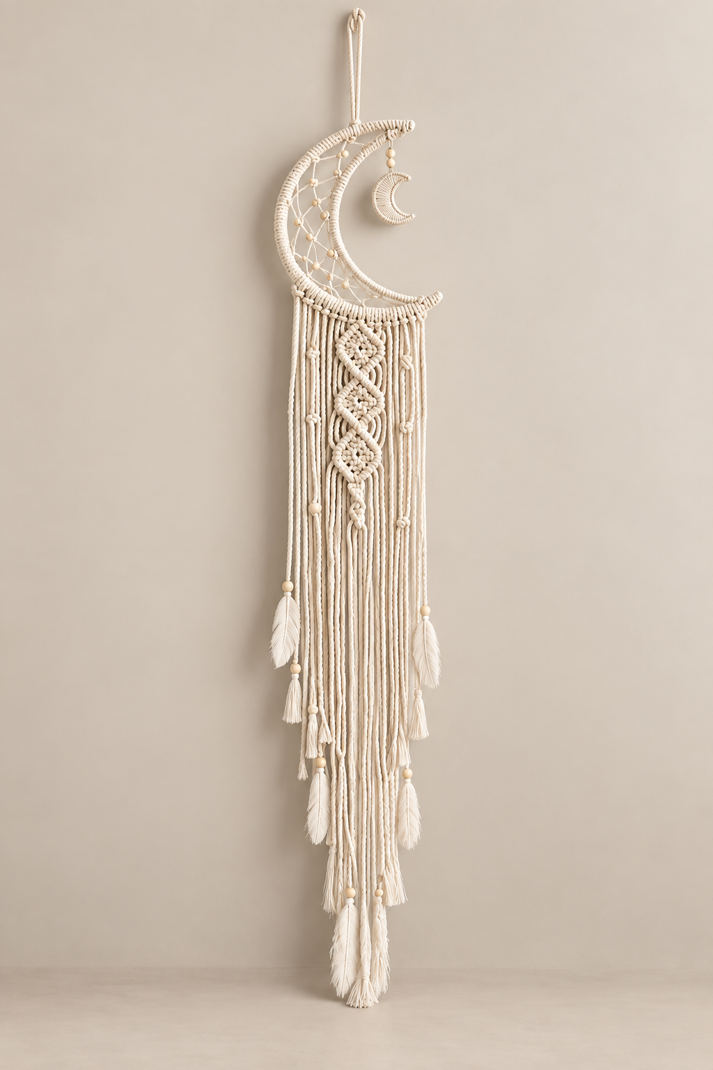Cream macrame moon dream catcher with feathers and beads, unlit, on a warm wall