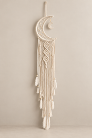Cream macrame moon dream catcher with feathers and beads, unlit, on a warm wall