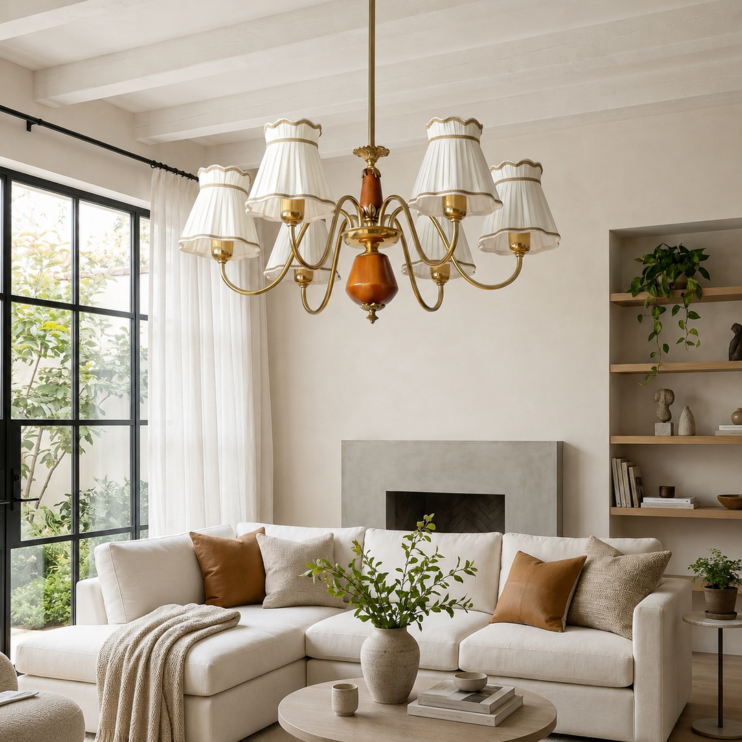 A brass six-light chandelier with white drum shades hangs in a bright, modern living room with a cream sectional sofa, fireplace, and shelving.